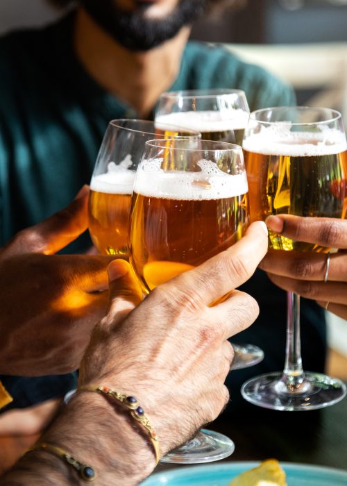 Close up of friends toasting with beer indoors. Friends having fun at bar cheering with beer.